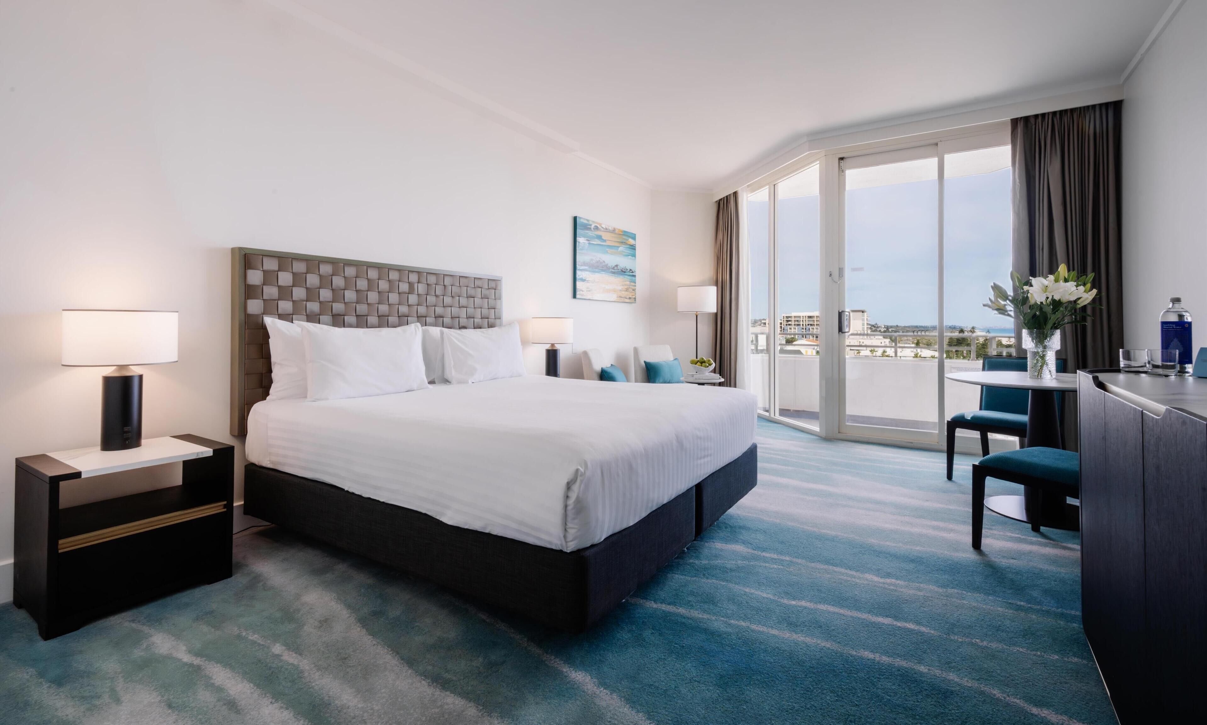 A hotel room with a large bed, a desk, a chair, and a balcony with a view.