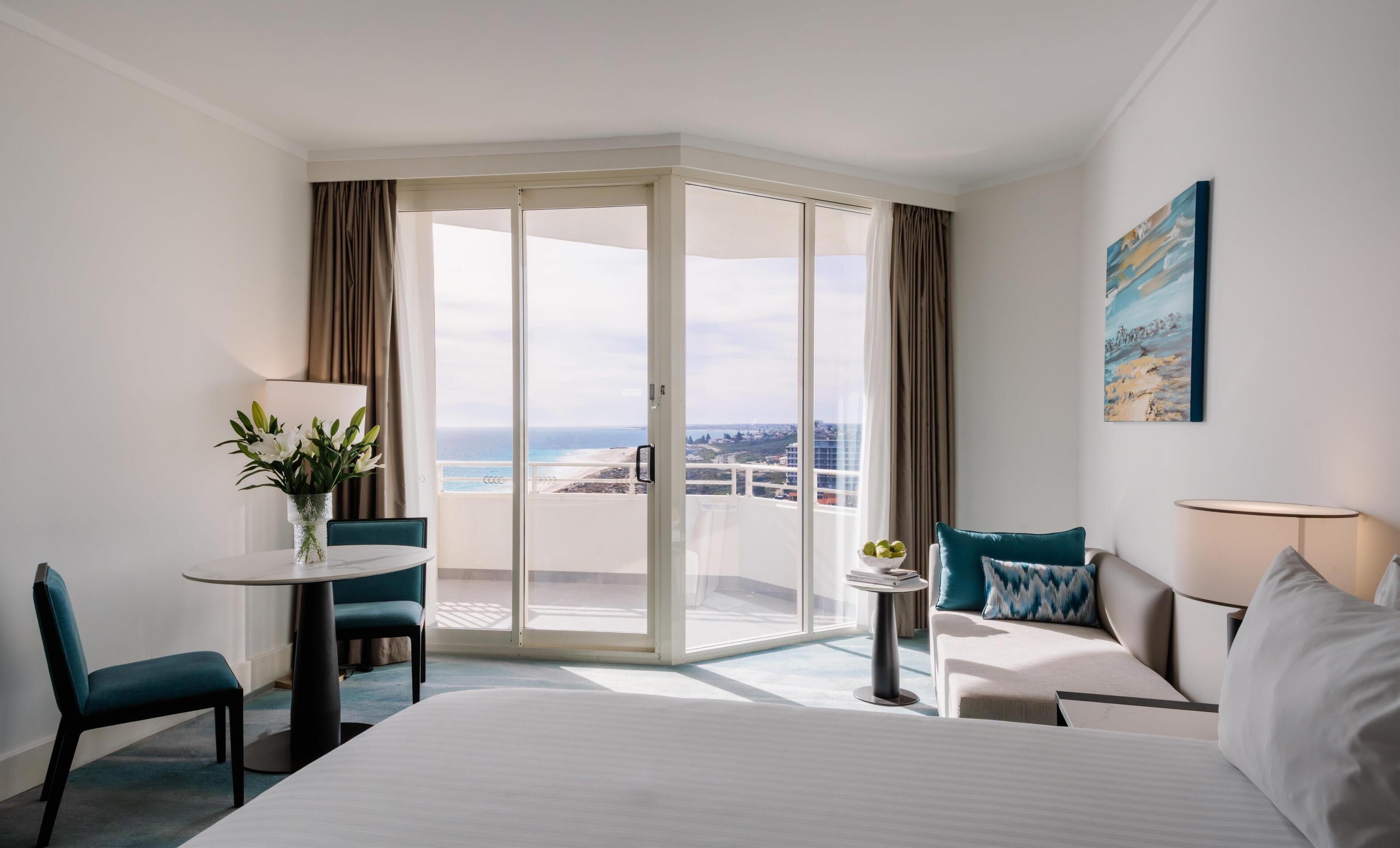 A hotel room with a bed, a desk, a chair, a small table, a sofa, and a view of the ocean.