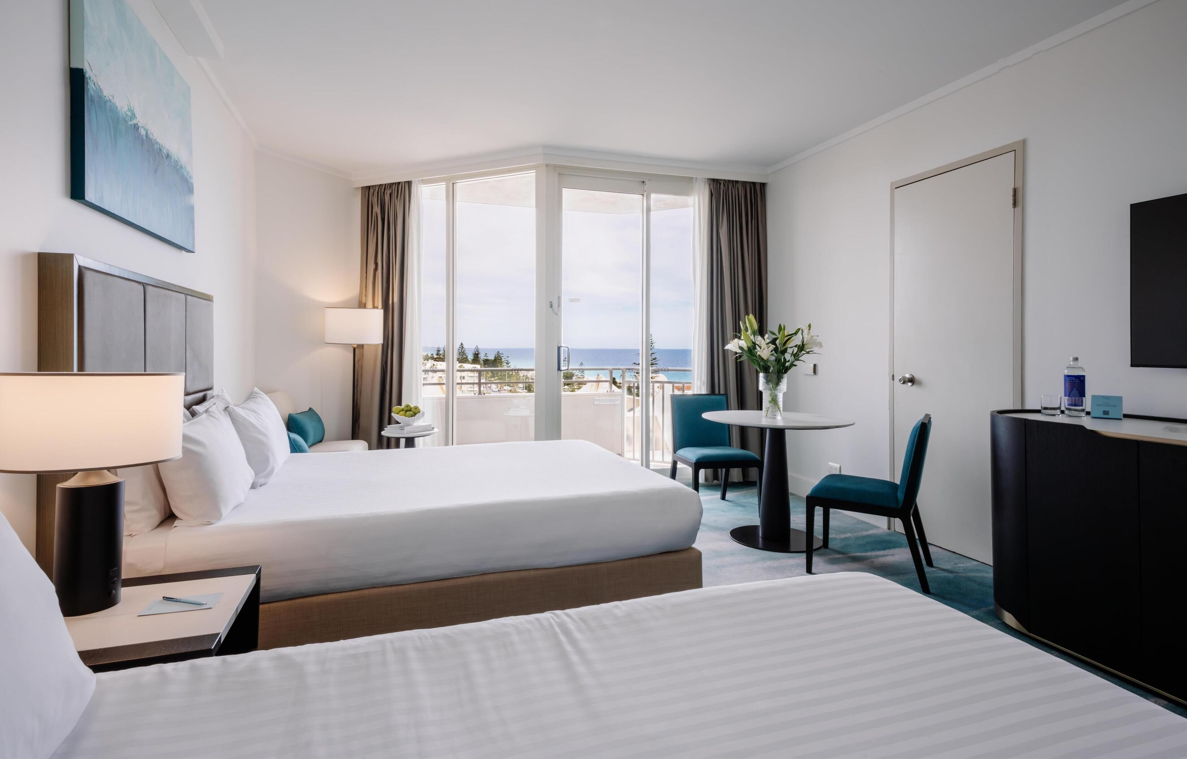 Habitación de hotel con dos camas, un escritorio, una silla, un televisor y un balcón con vistas al mar.