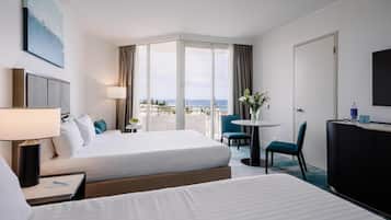Habitación de hotel con dos camas, un escritorio, una silla, un televisor y un balcón con vistas al mar.