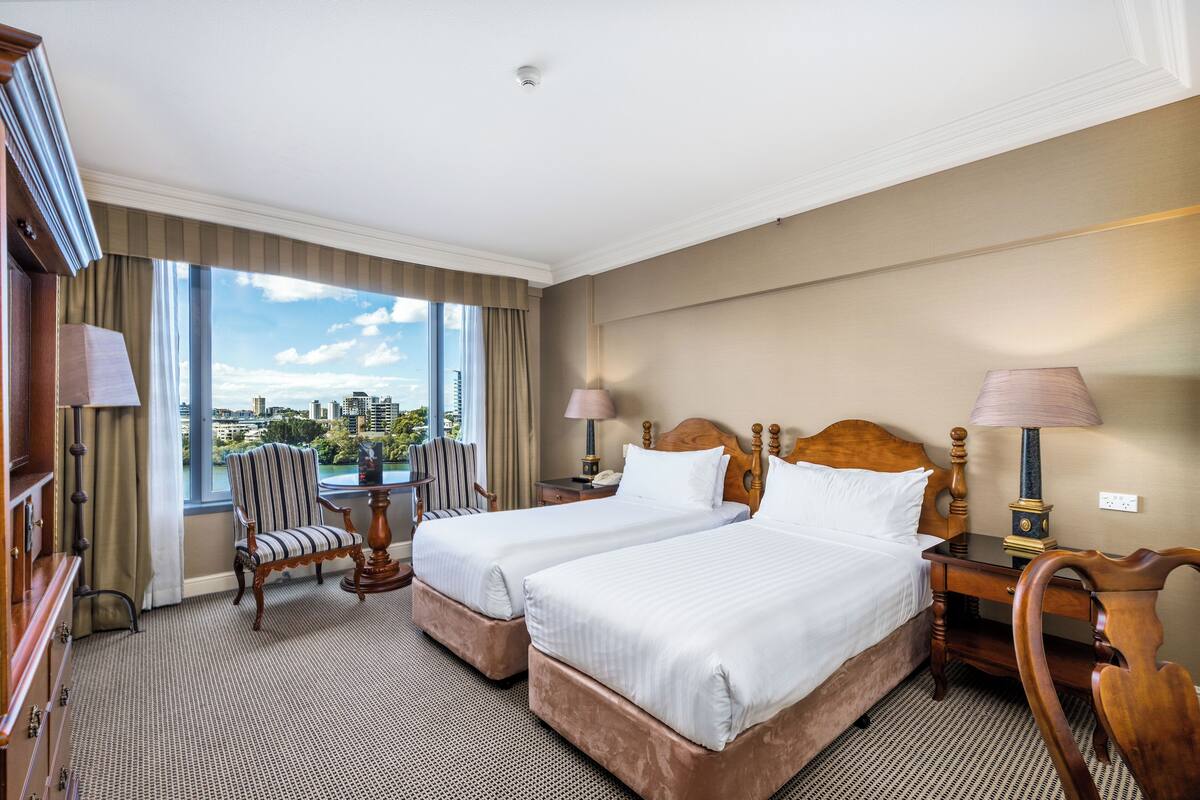 Een hotelkamer met twee bedden, uitzicht op de stad, een stoel en een bureau met een lamp.