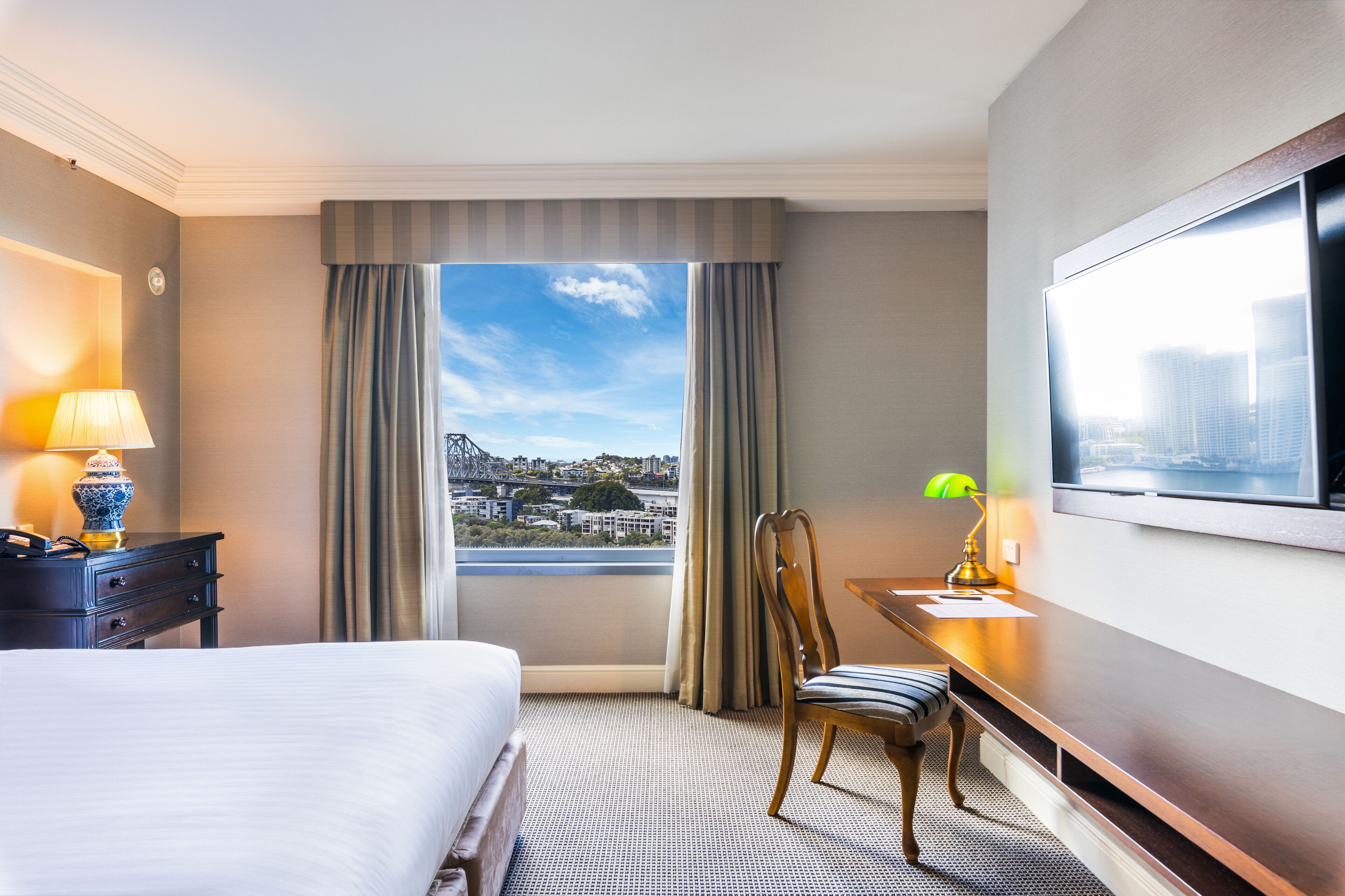 A hotel room with a bed, a desk, a chair, a TV, and a window with a city view.