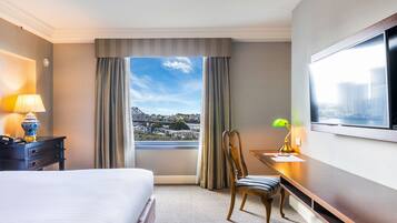 A hotel room with a bed, a desk, a chair, a TV, and a window with a city view.