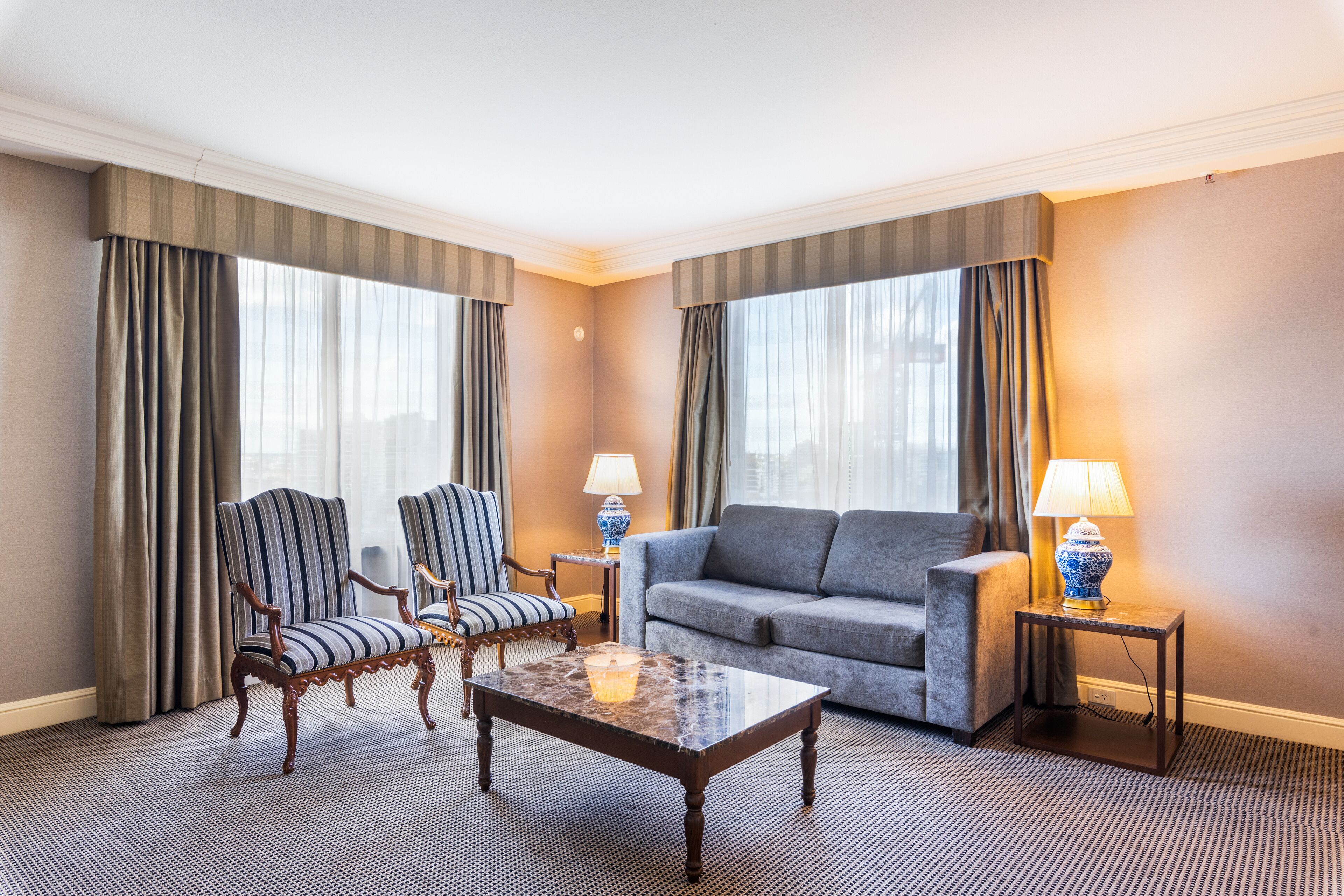 A hotel room with a sofa, two armchairs, a coffee table, and a lamp on a side table.