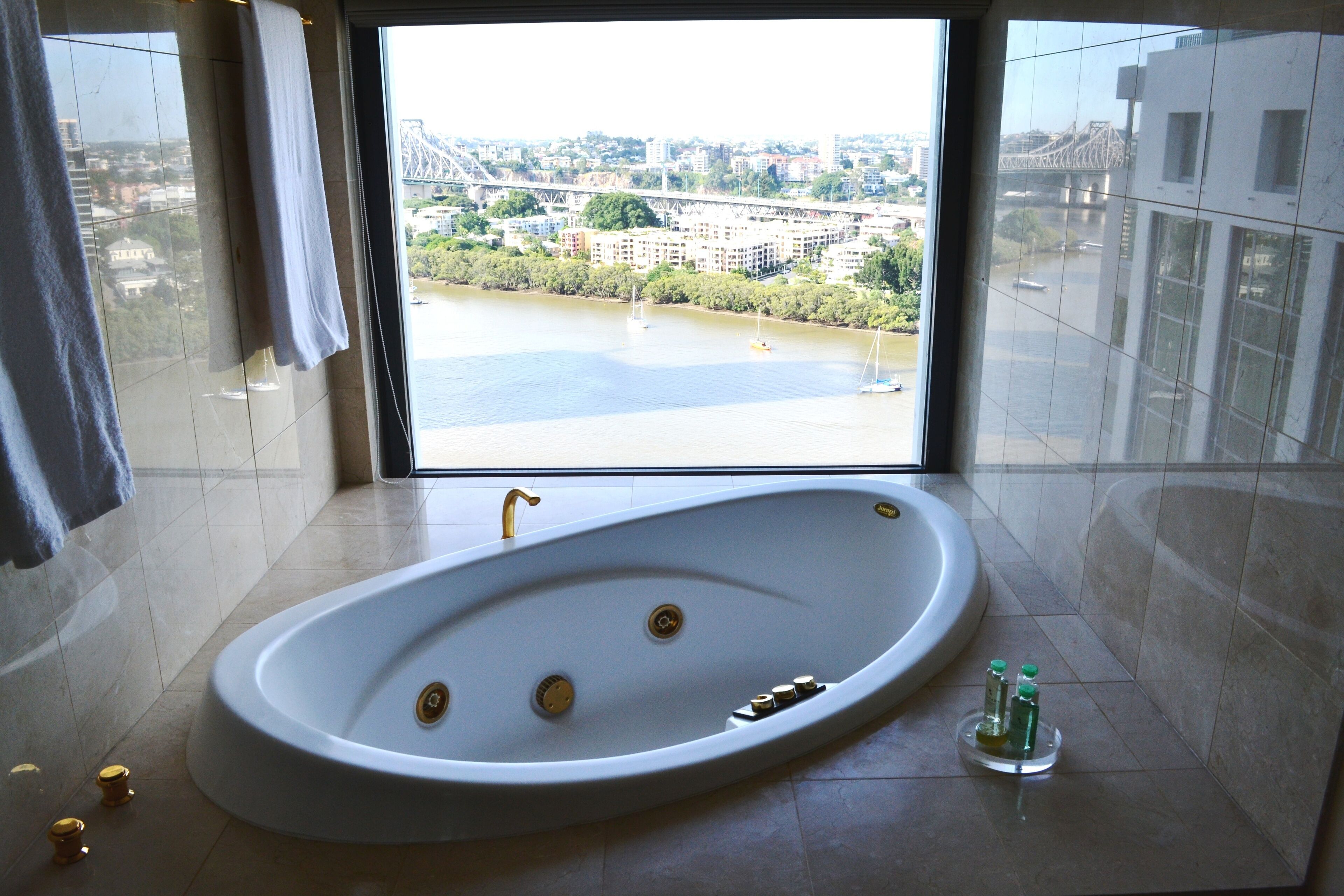 A modern bathroom with a large bathtub, a view of a cityscape, and a window with curtains.