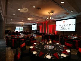 Un salón de banquetes con mesas redondas, cintas rojas y candelabros.