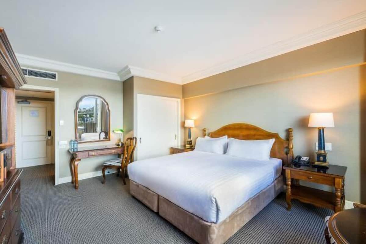 Een hotelkamer met een groot bed, nachtkastjes, een bureau en een spiegel.