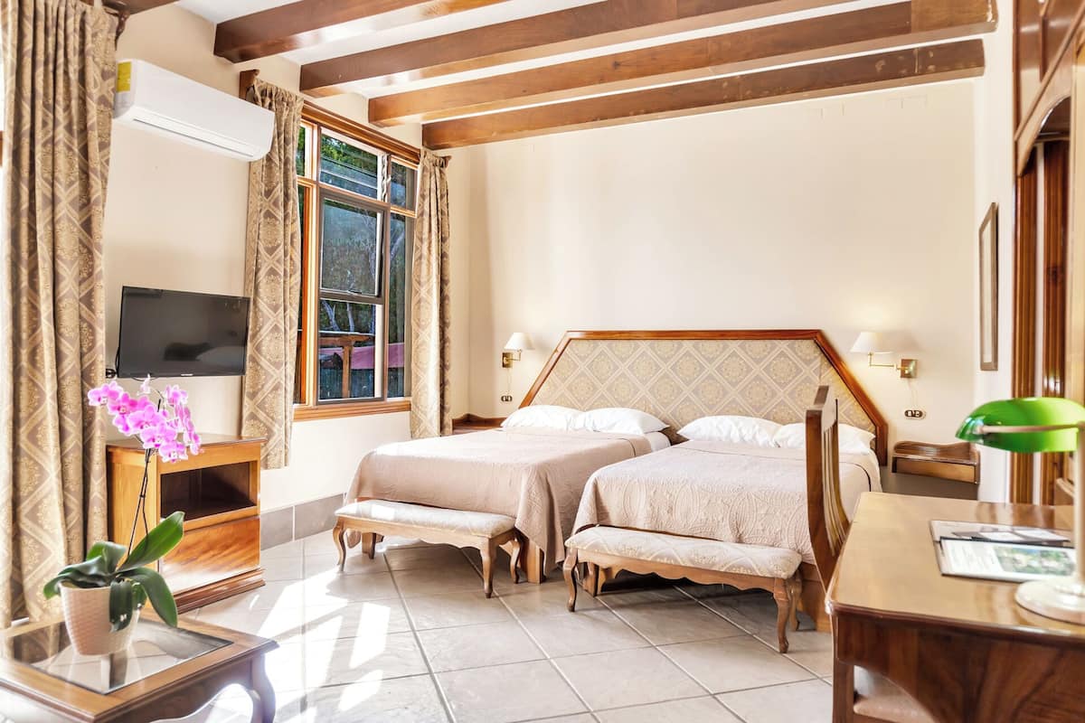 A hotel room with two beds, a TV, a desk, and a window with curtains.