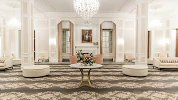 Um hall imponente com piso de mármore, uma mesa redonda central e um lustre.