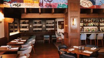 A restaurant with wooden tables and chairs, a bar area with shelves of bottles, and a mural on the ceiling.