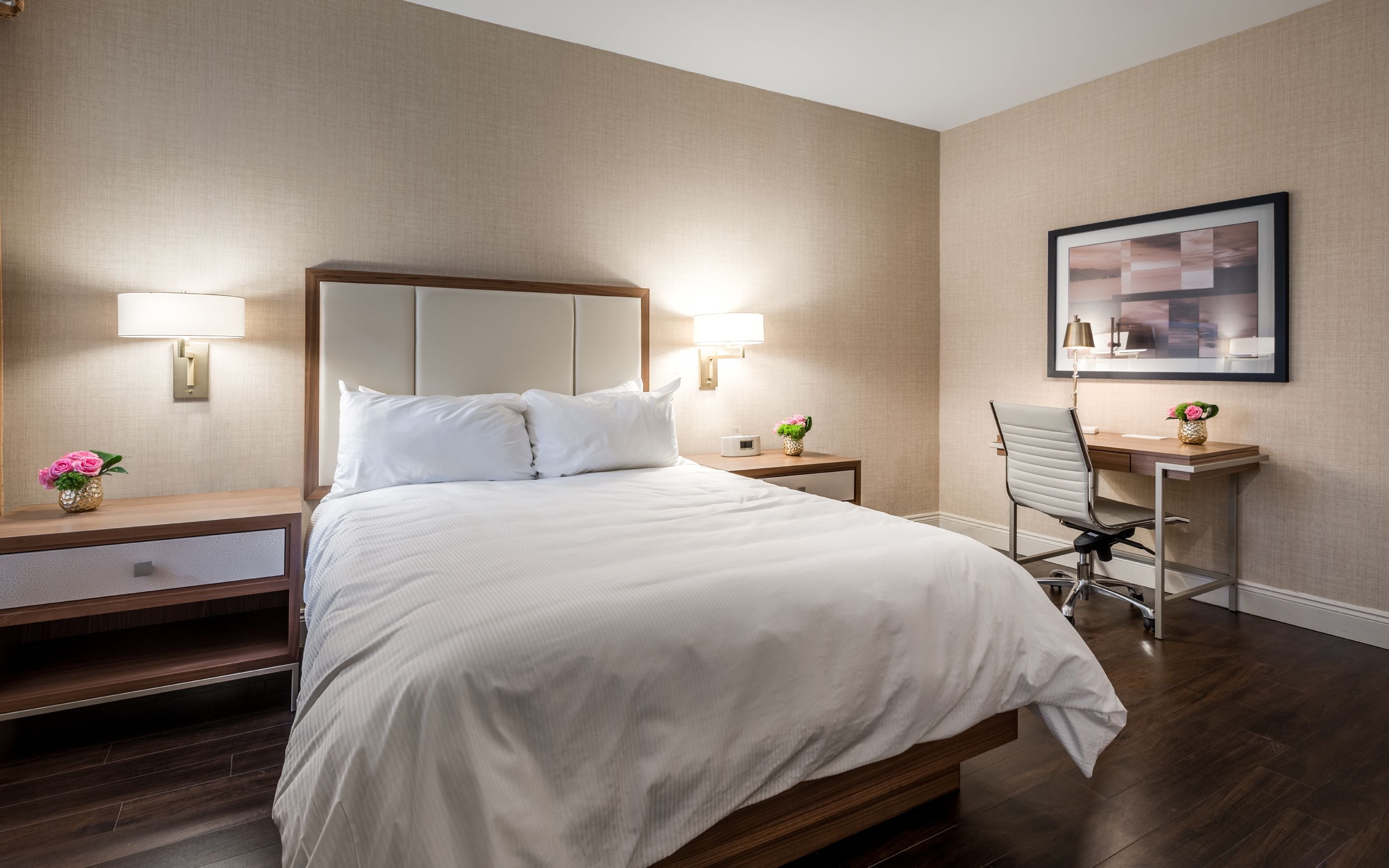 A hotel room with a large bed, two bedside lamps, a desk with a chair, and a framed picture on the wall.