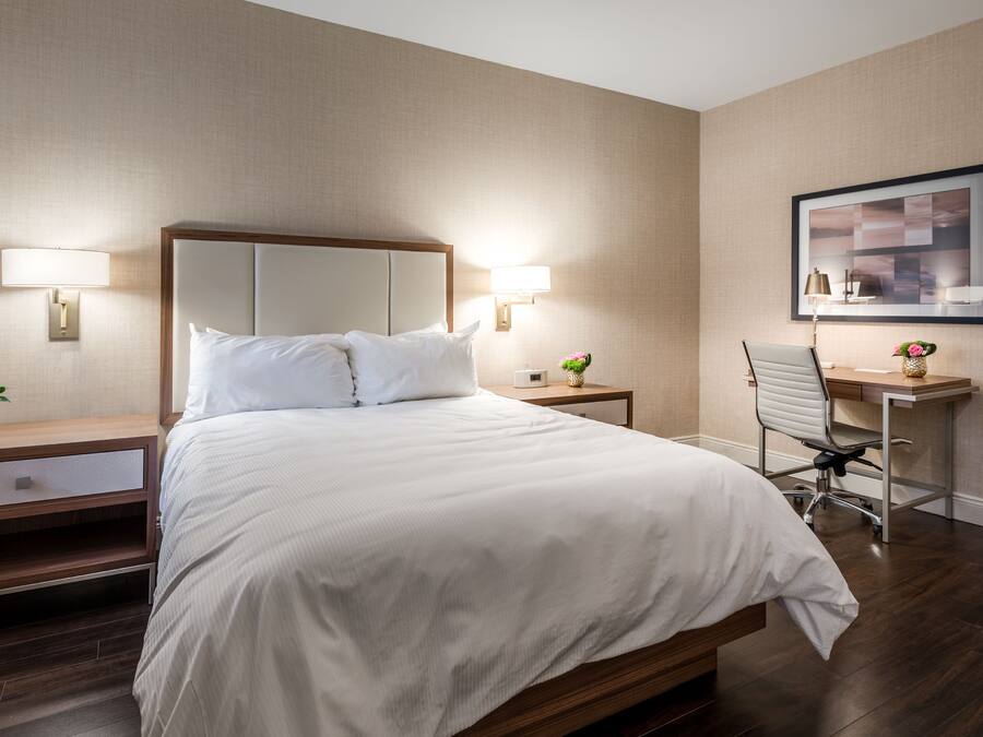 A hotel room with a large bed, two bedside lamps, a desk with a chair, and a framed picture on the wall.