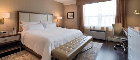 Une chambre d’hôtel avec un grand lit, une banquette, un bureau, une chaise et une fenêtre avec des rideaux.