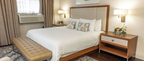 Quarto de hotel com cama grande, um banco, mesa de cabeceira e luminária na parede.