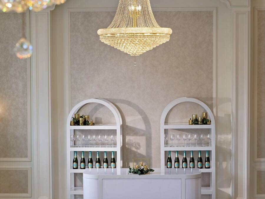 A formal dining area with a chandelier, white buffet with wine bottles, and elegant chairs.