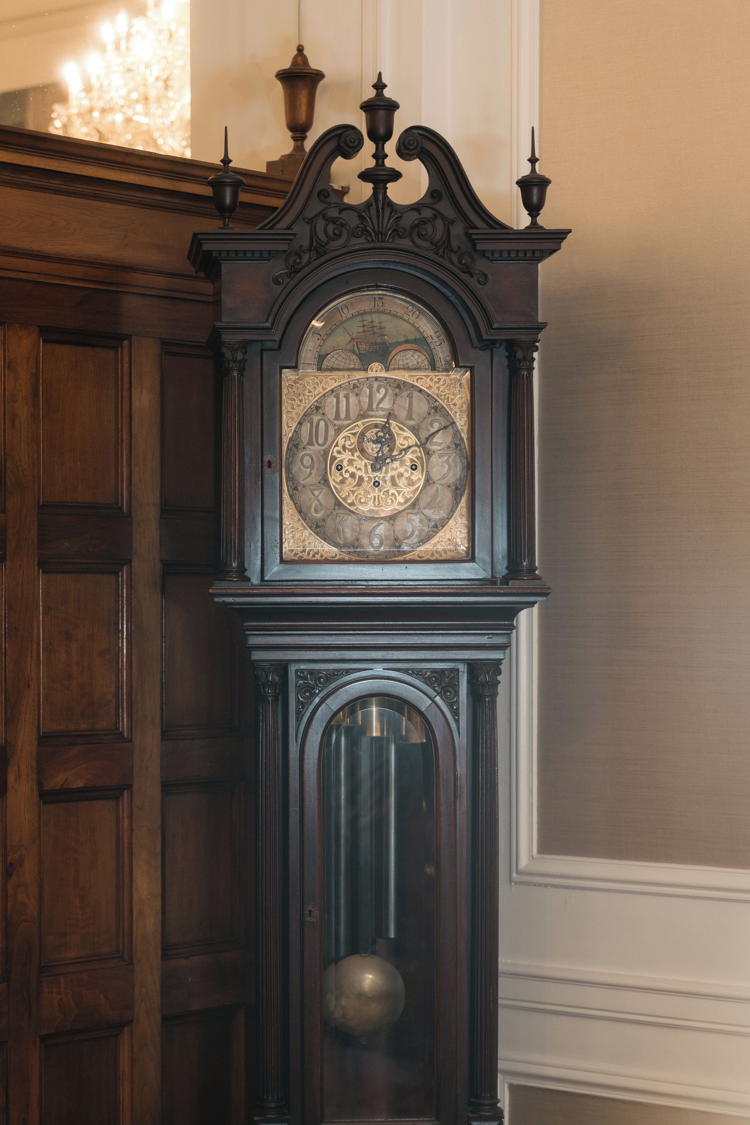 Un reloj de pie antiguo con tallas elaboradas y un péndulo visible a través del vidrio.