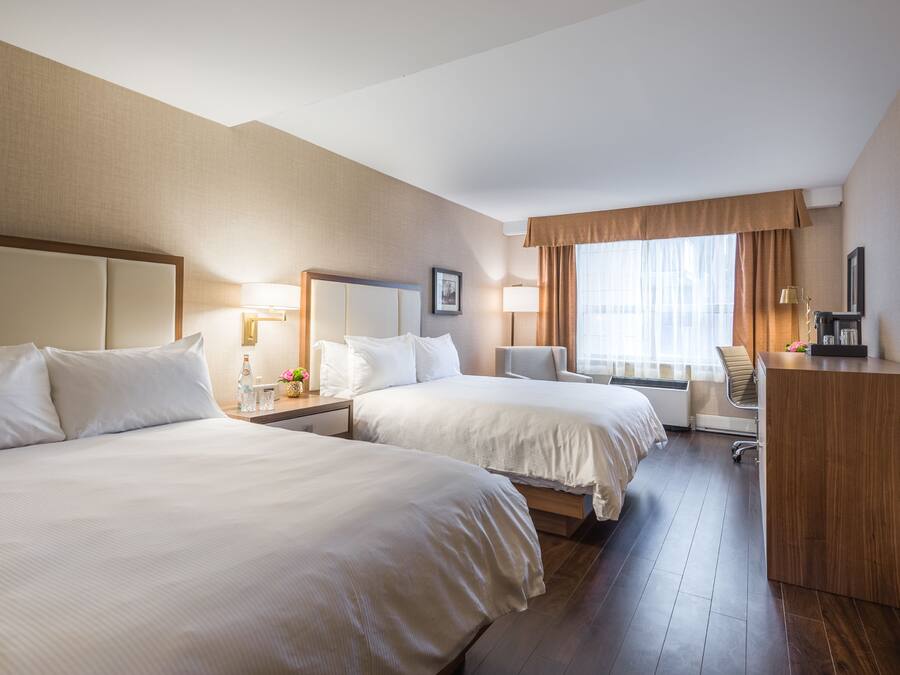 Habitación de hotel con dos camas, un escritorio, una silla, un televisor y un ventanal con cortinas.