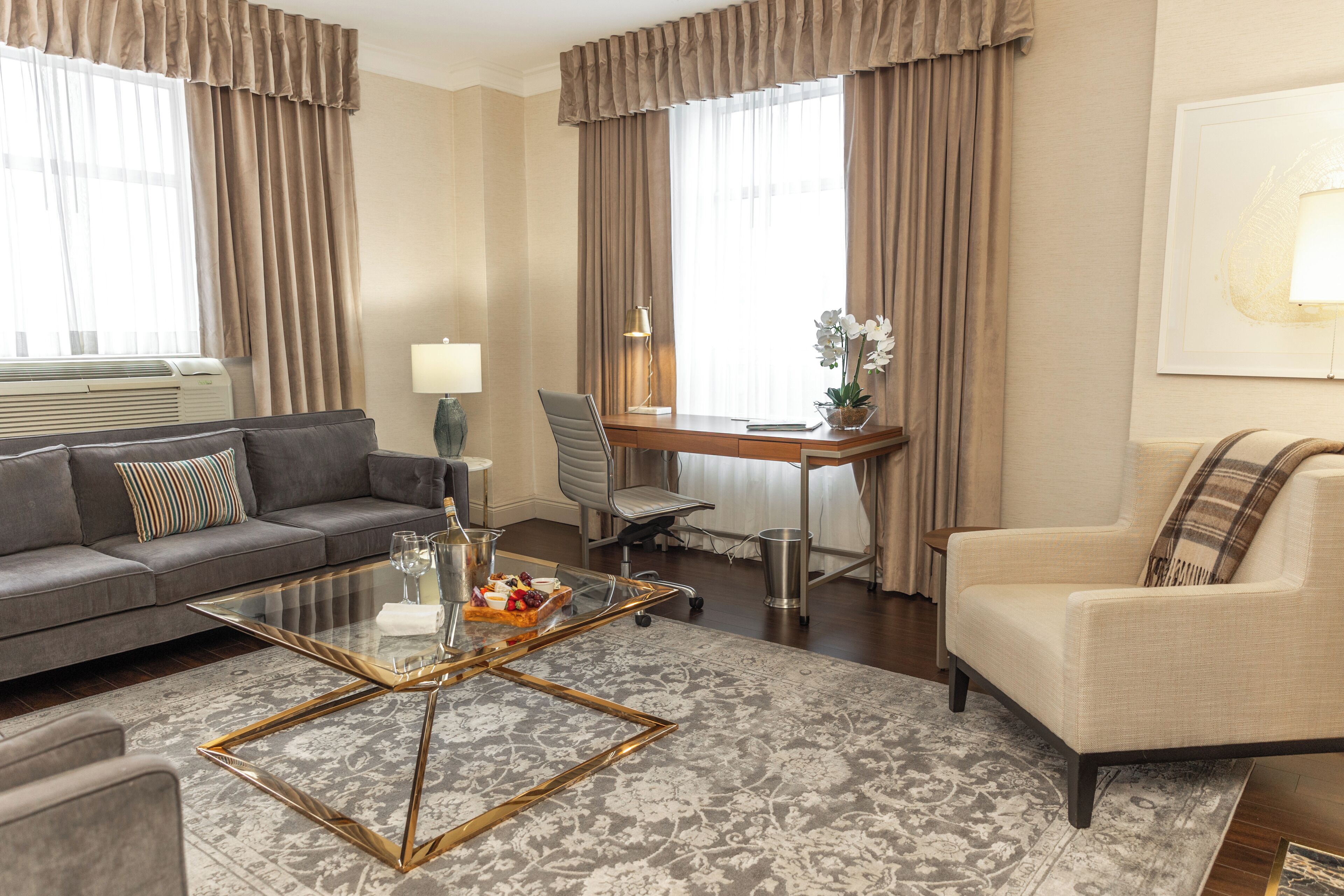 A modern living room with a sofa, armchair, glass coffee table, and a desk with a lamp.