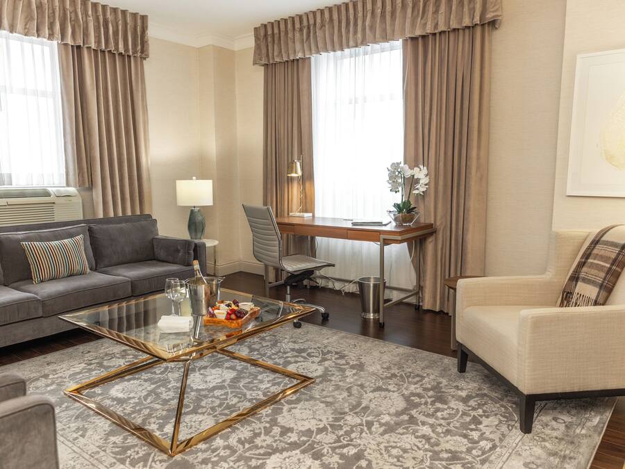 A modern living room with a sofa, armchair, glass coffee table, and a desk with a lamp.