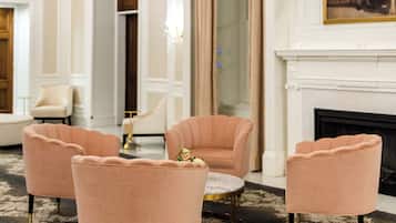 Une pièce avec une cheminée, un tableau et quatre fauteuils roses disposés autour d’une petite table.