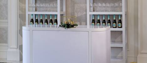 A formal dining setup with a white table, gold-accented chairs, and a white bar area with wine bottles and glasses.