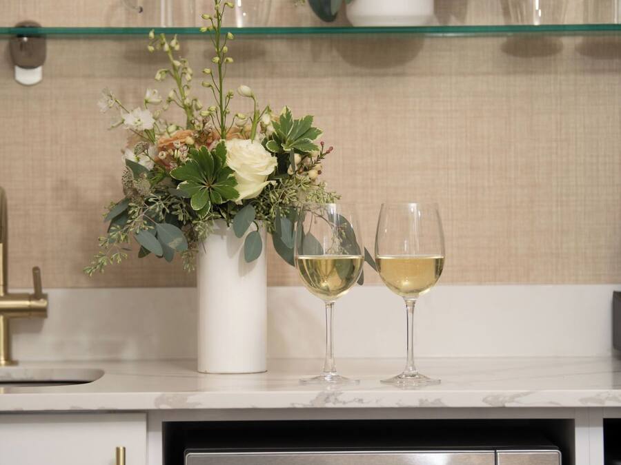 A kitchen with a microwave, two wine glasses, and a vase with flowers on a shelf.