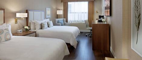 A hotel room with two beds, a desk, a chair, a window with curtains, a coffee maker, and a decorative feather on the wall.