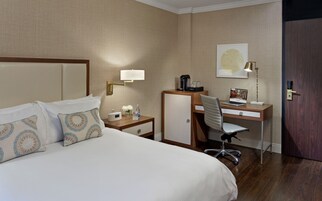 Una habitación de hotel con cama, escritorio, silla, cafetera, reloj y puerta.