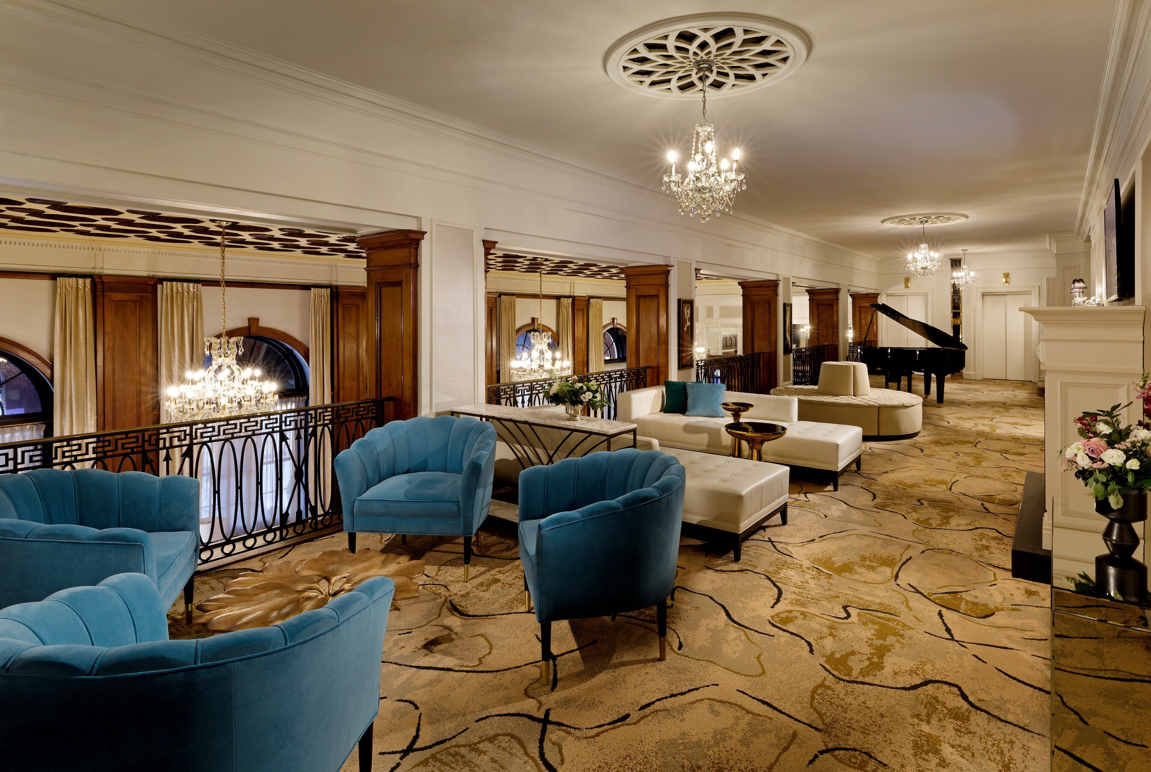 A spacious lobby with a grand piano, elegant blue armchairs, a fireplace, and a chandelier.