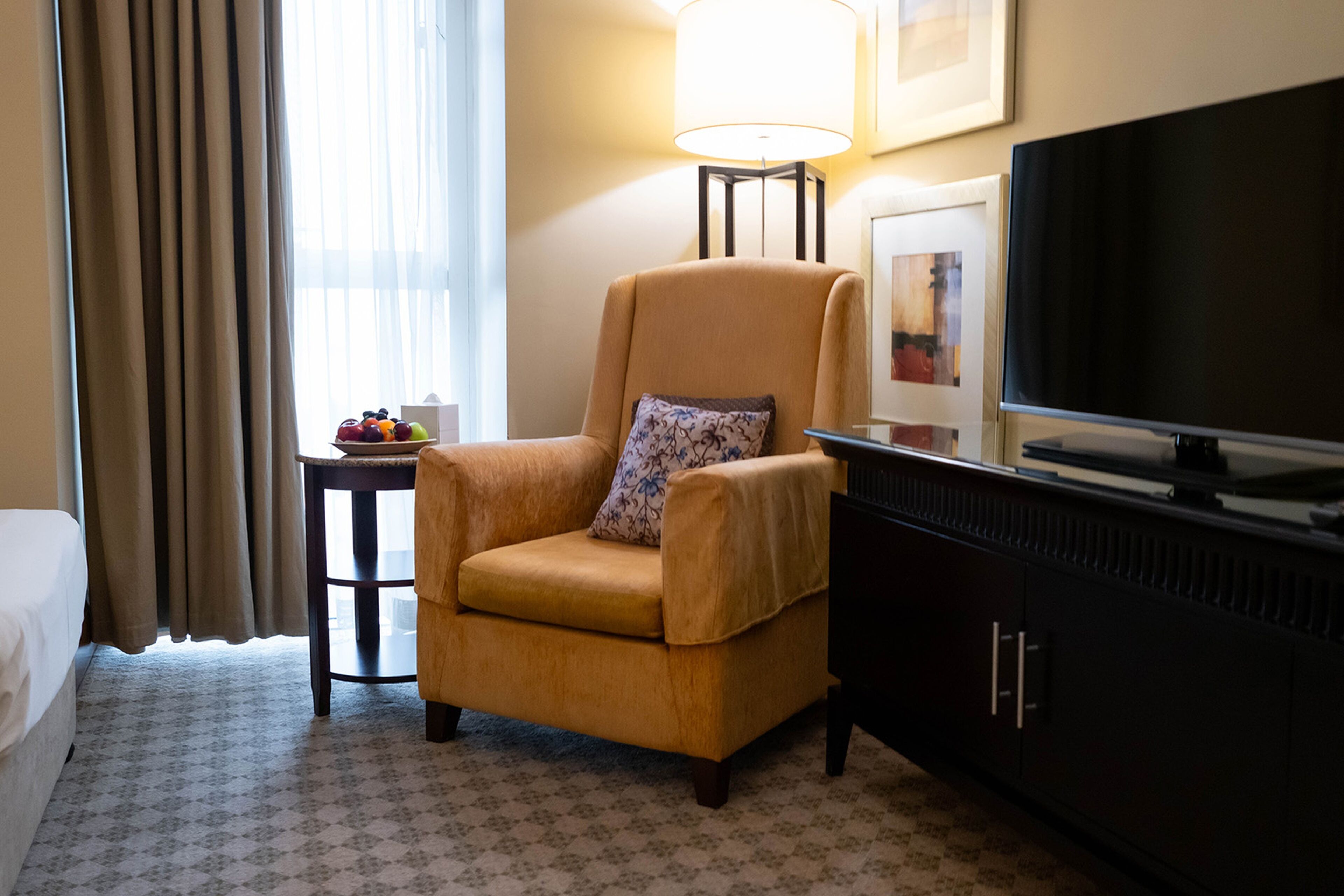 Ein Hotelzimmer mit Sofa, einem kleinen Tisch mit Obst, einer Lampe, einem Fernseher und einem Bett.