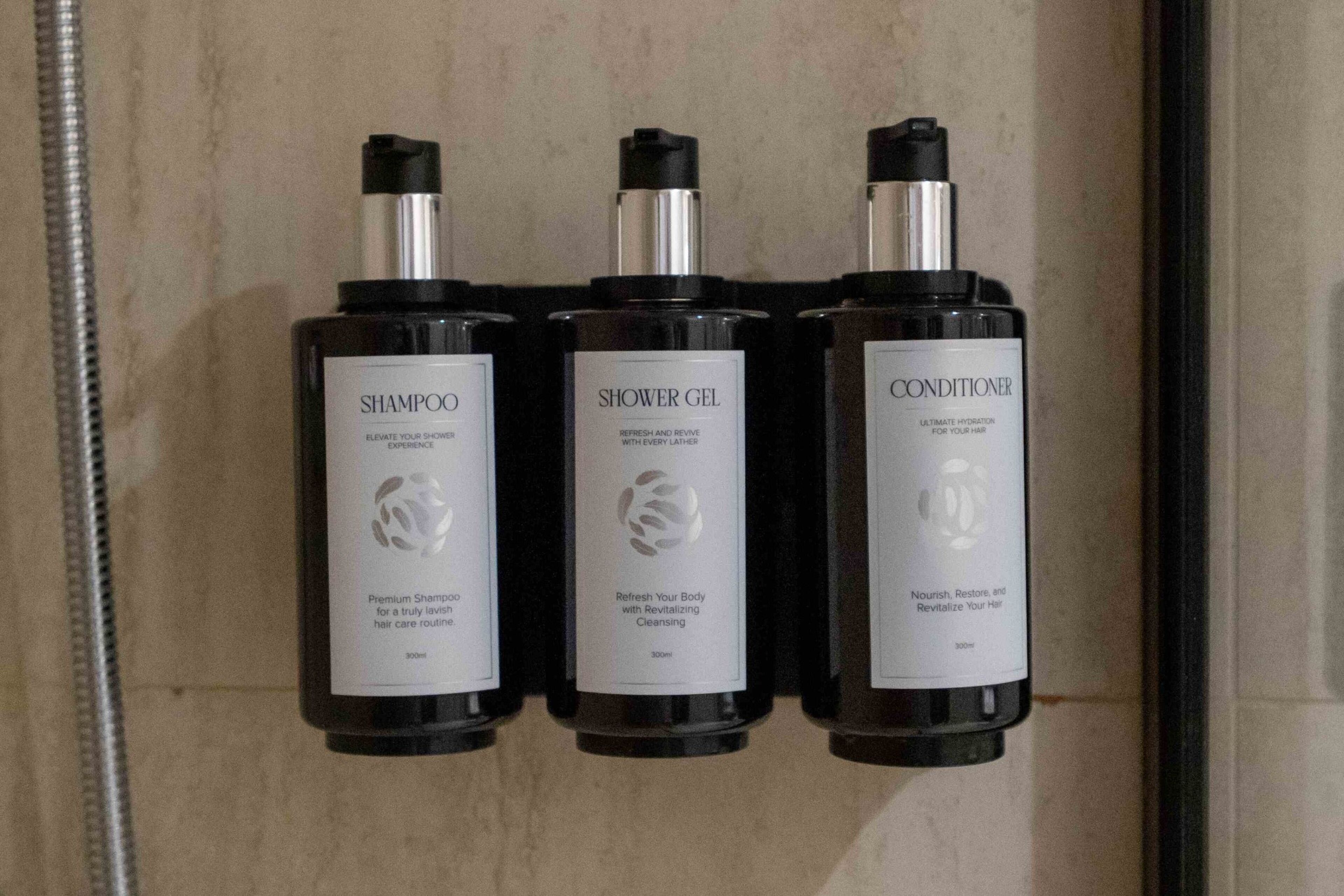 Tre flasker hårplejeprodukter: shampoo, shower gel og conditioner, hver mærket med deres anvendelse og fordele.