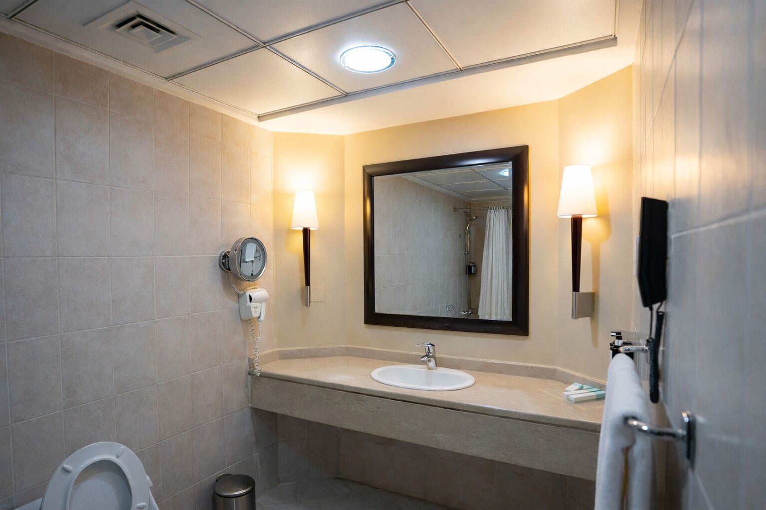 Un baño moderno con inodoro, lavamanos y espejo. Cuenta con un perchero y un cubo de basura.