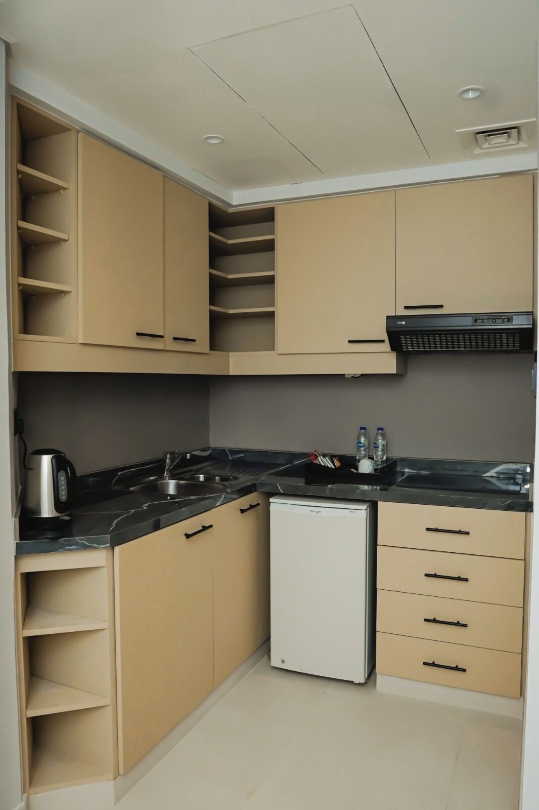A compact kitchen with beige cabinetry, a black countertop, and a built-in dishwasher.