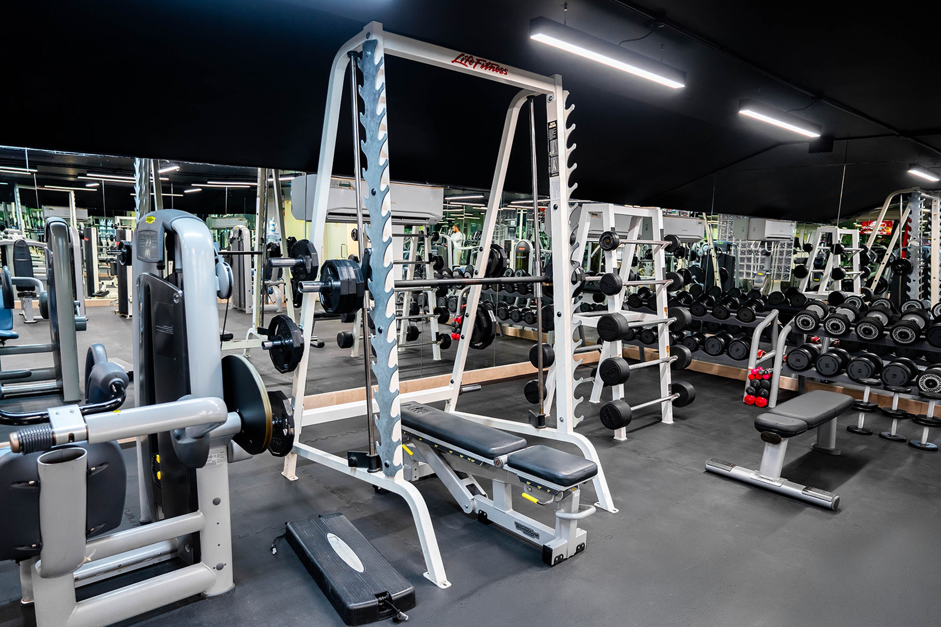 A gym with various weightlifting equipment, benches, and dumbbells.
