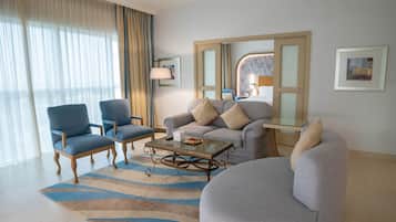 A modern hotel room with a sofa, two armchairs, a coffee table, and a glass side table.