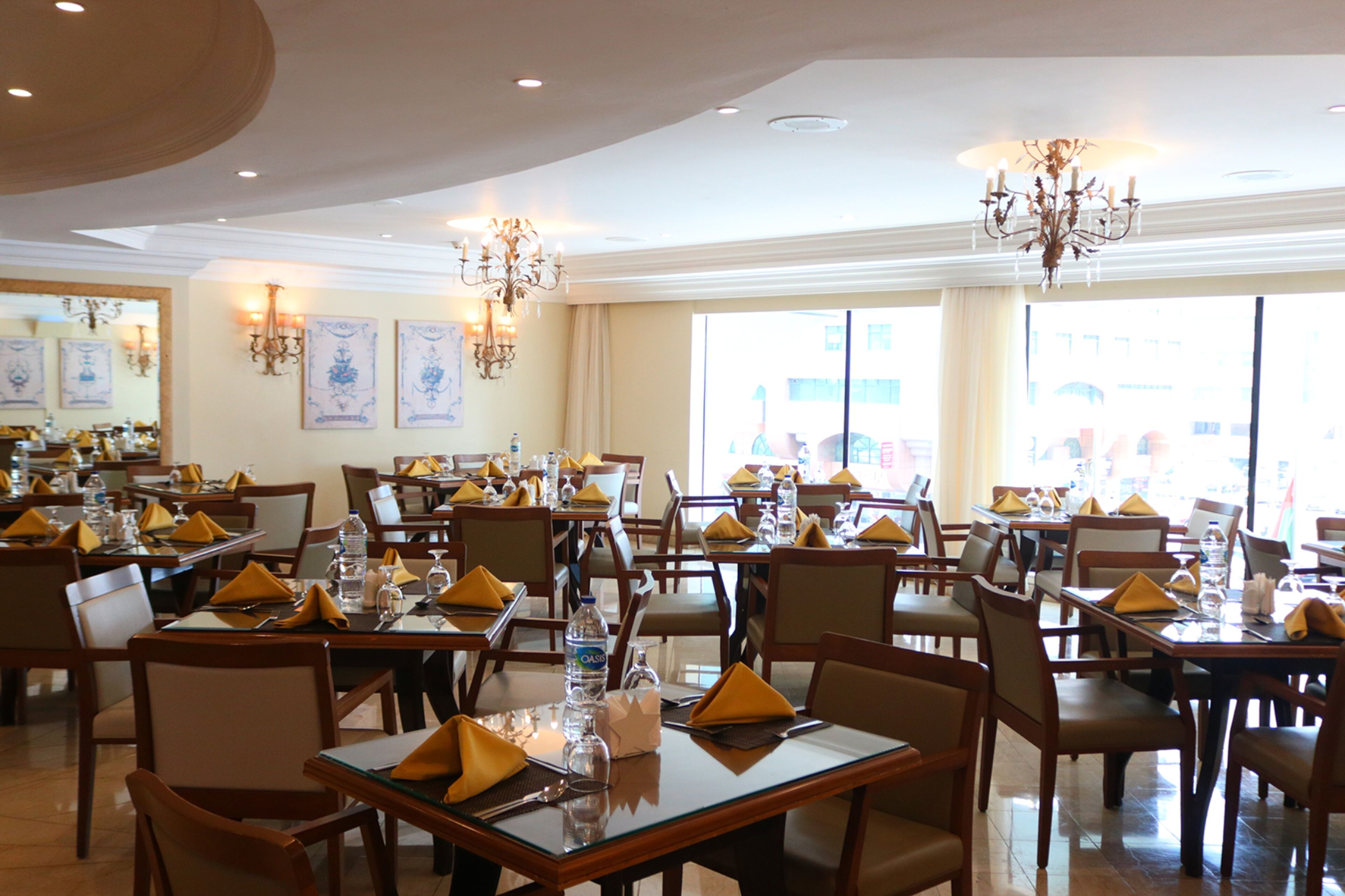 Un restaurant avec de nombreuses tables, chacune mise avec des serviettes jaunes, des bouteilles d’eau et des verres.