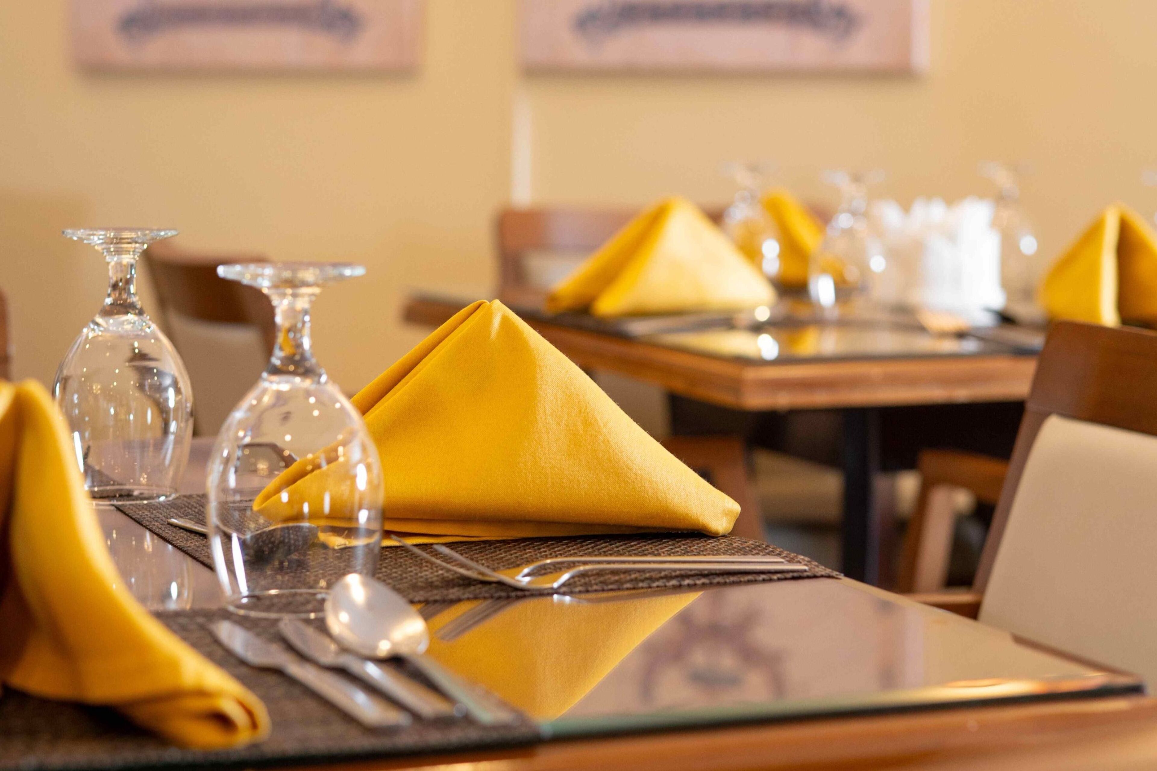 A dining table set with yellow napkins, clear wine glasses, and cutlery.