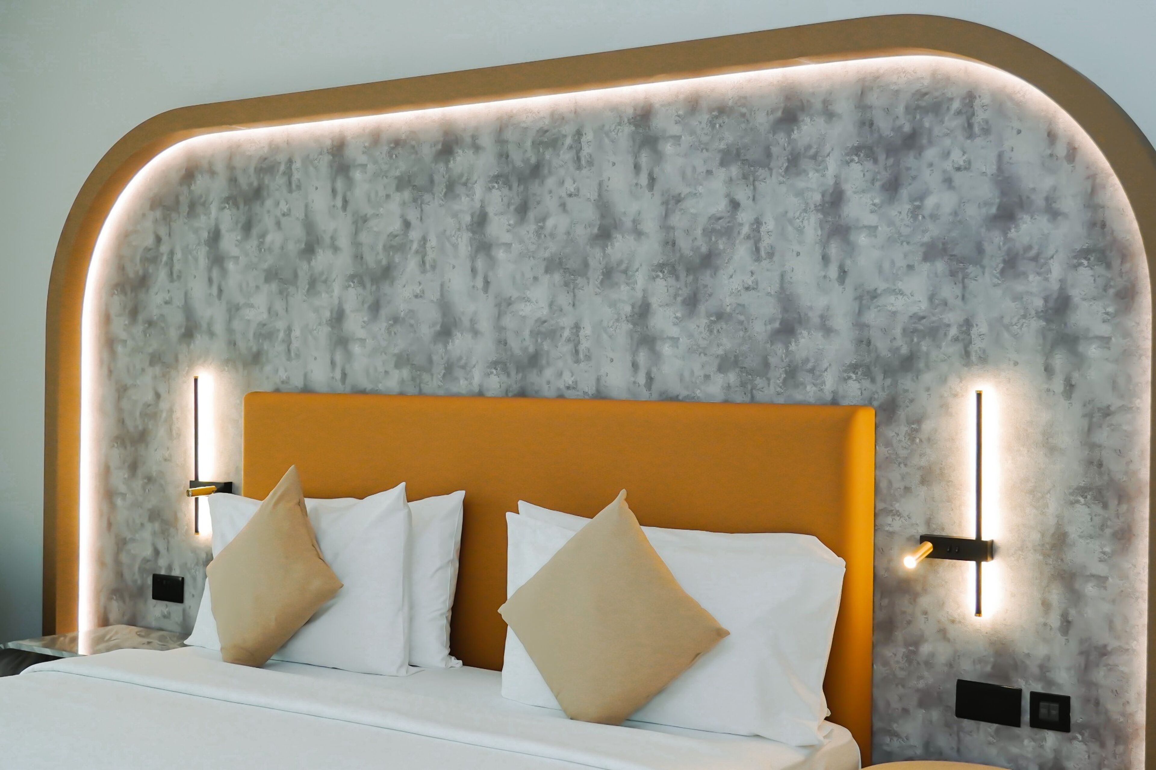 A modern hotel room with a marble-patterned headboard, white bedding, and two wall-mounted light fixtures.