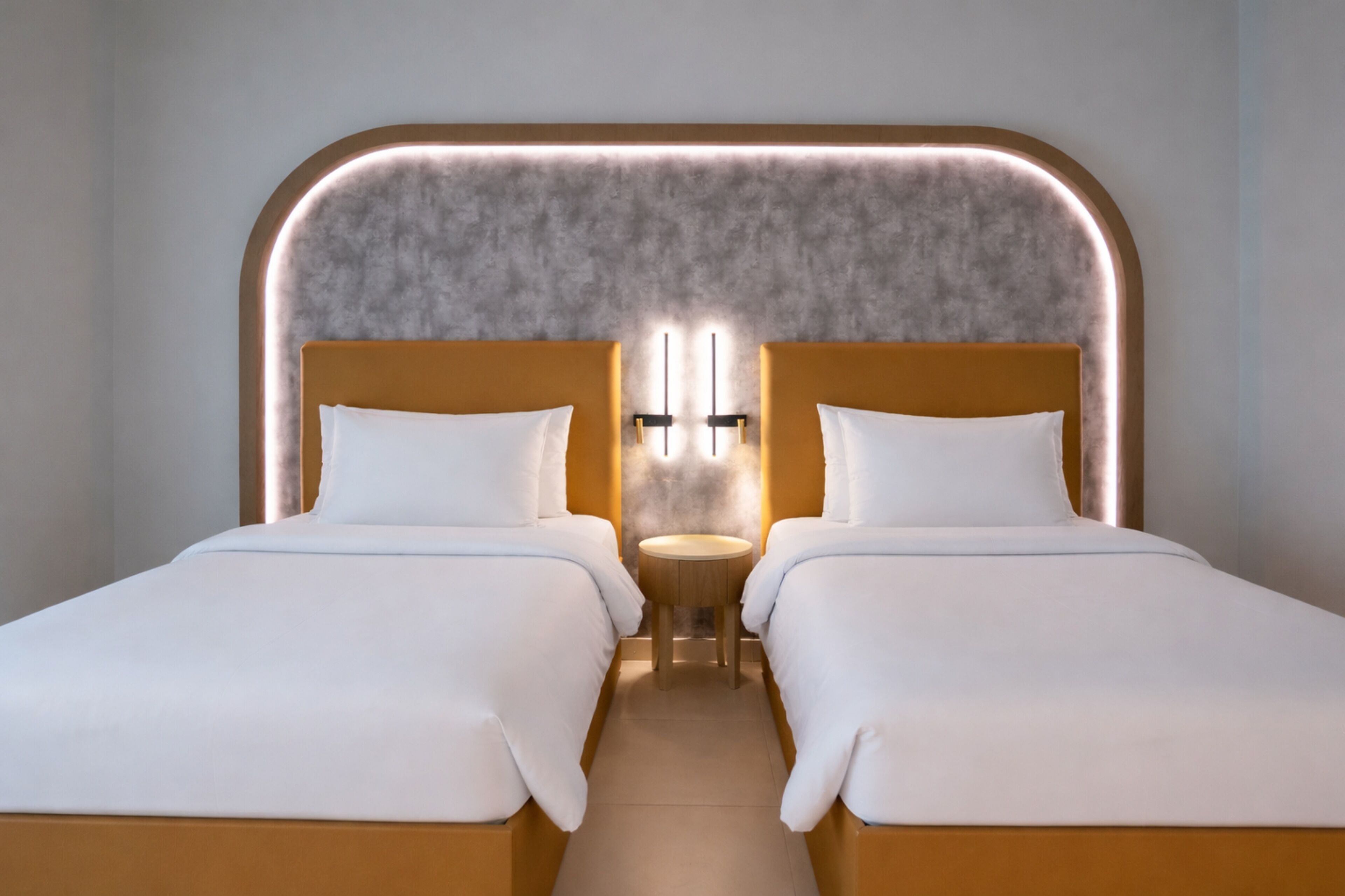 Una cama doble con cabecera que incluye un panel iluminado, una mesita de noche y un aplique de pared.