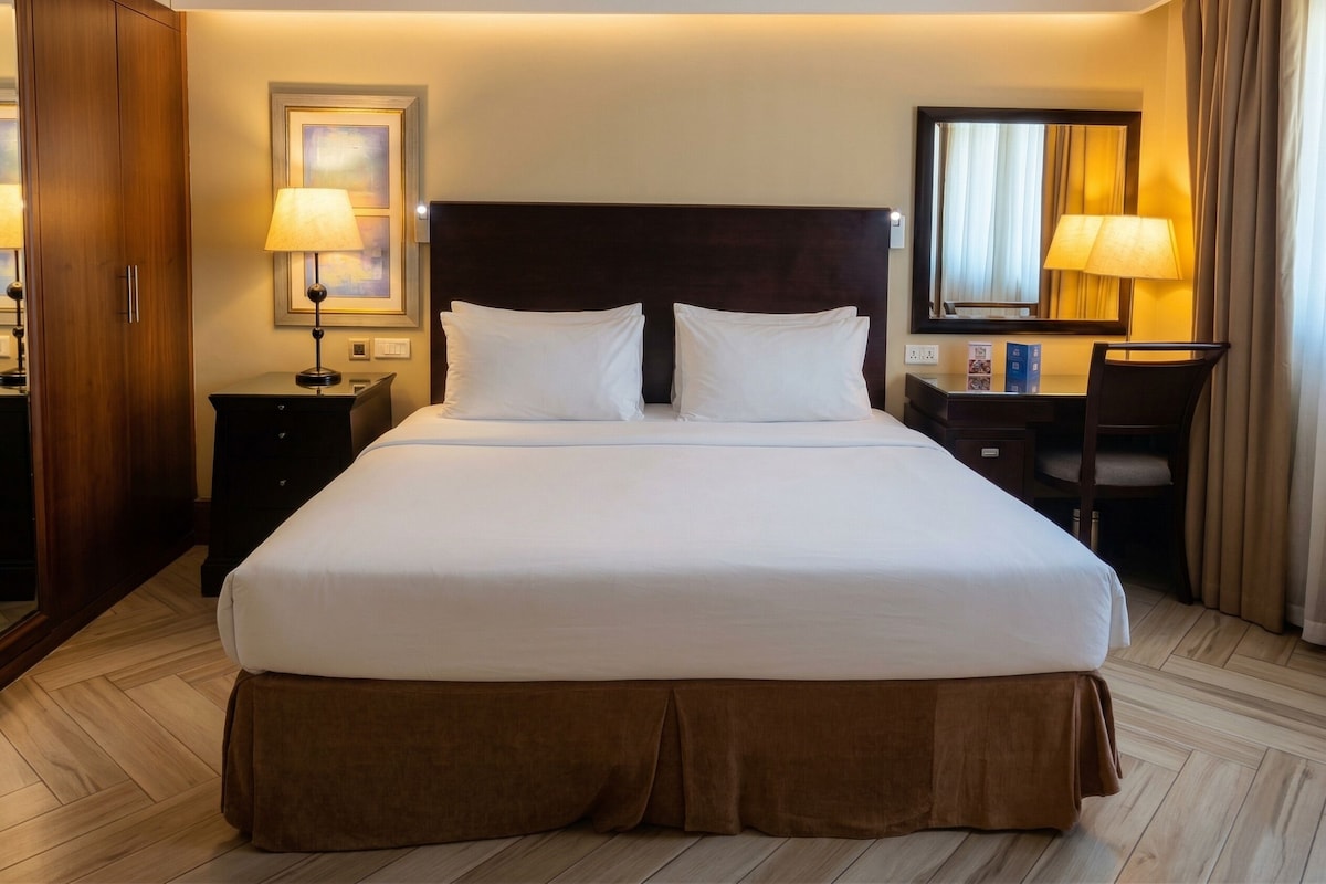 Habitación de hotel con una cama grande, cabecera de madera, escritorio con silla, lámpara y espejo.