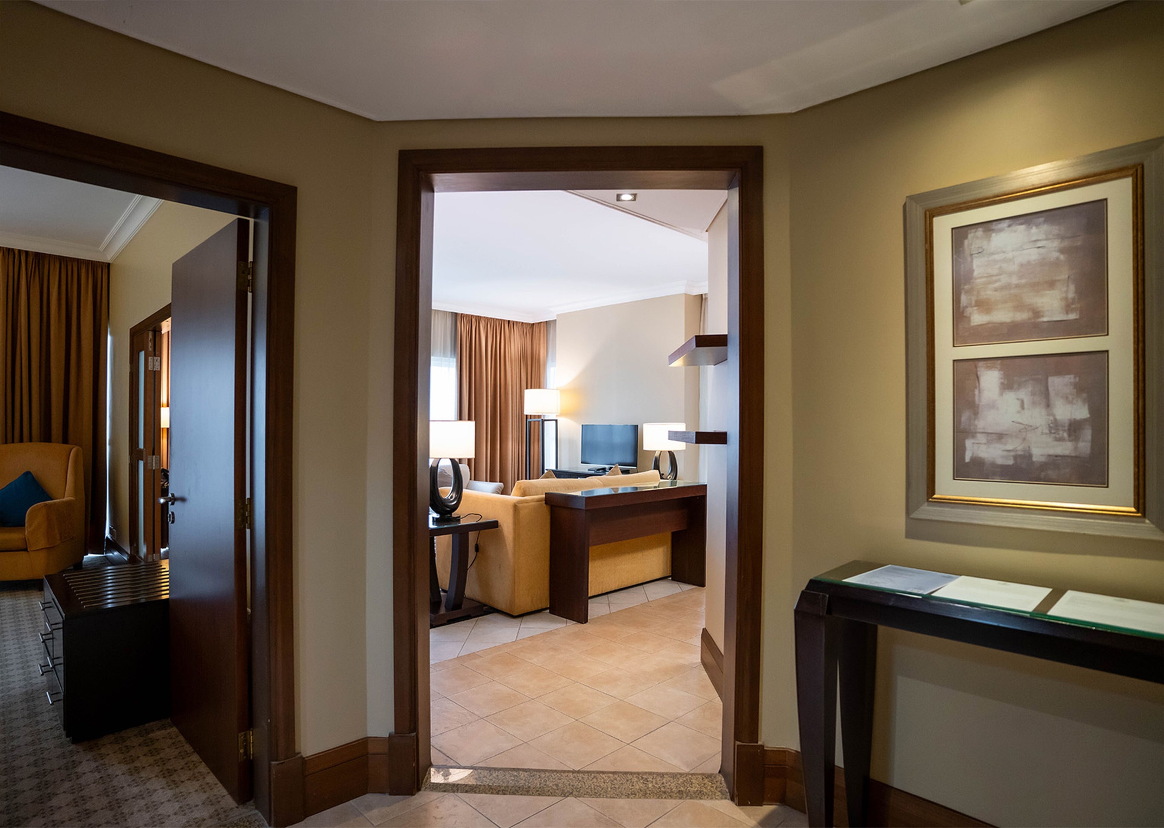 Ein Hotelzimmer mit Schreibtisch, Stuhl und Fernseher. Eine Tür führt in einen weiteren Raum.