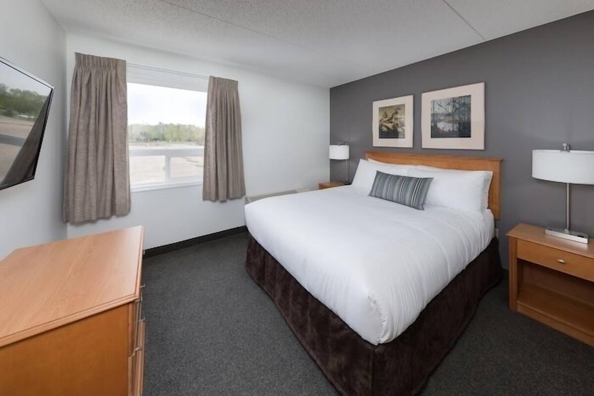 Une chambre d’hôtel avec un grand lit, deux tables de chevet, un bureau et une fenêtre avec des rideaux.