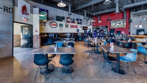 A spacious cafeteria with multiple tables and chairs, a variety of food and drink advertisements on the walls, and a visible entrance to a restaurant.