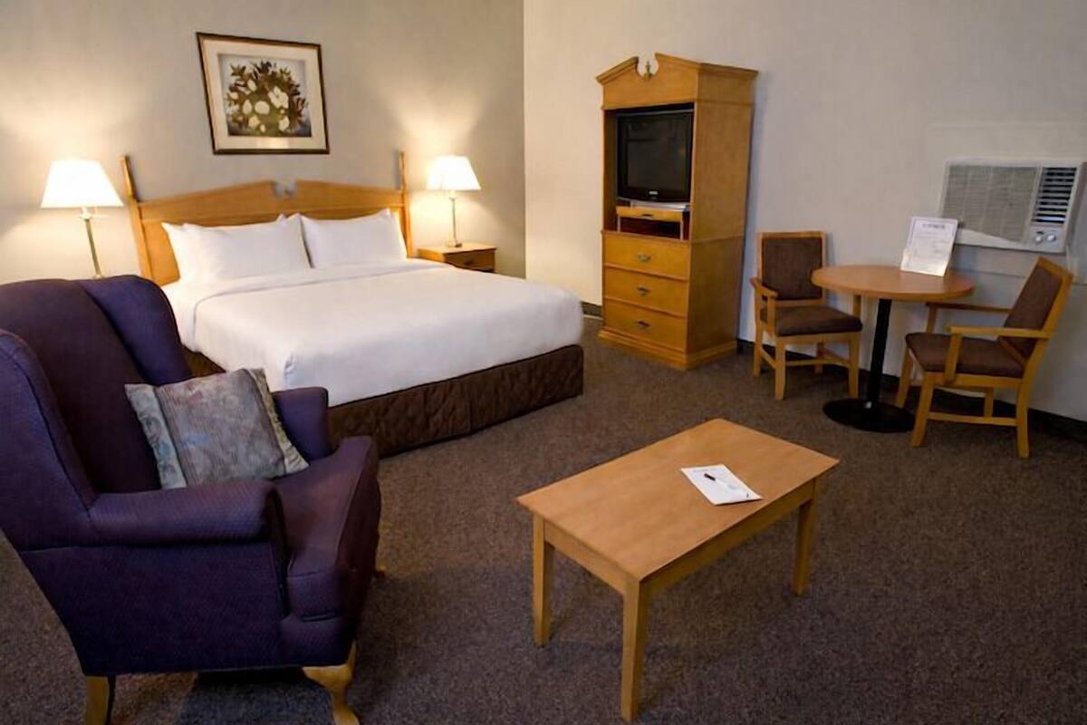 Une chambre d’hôtel comprenant un lit, un canapé, une table en bois, une télévision et un bureau avec deux chaises.