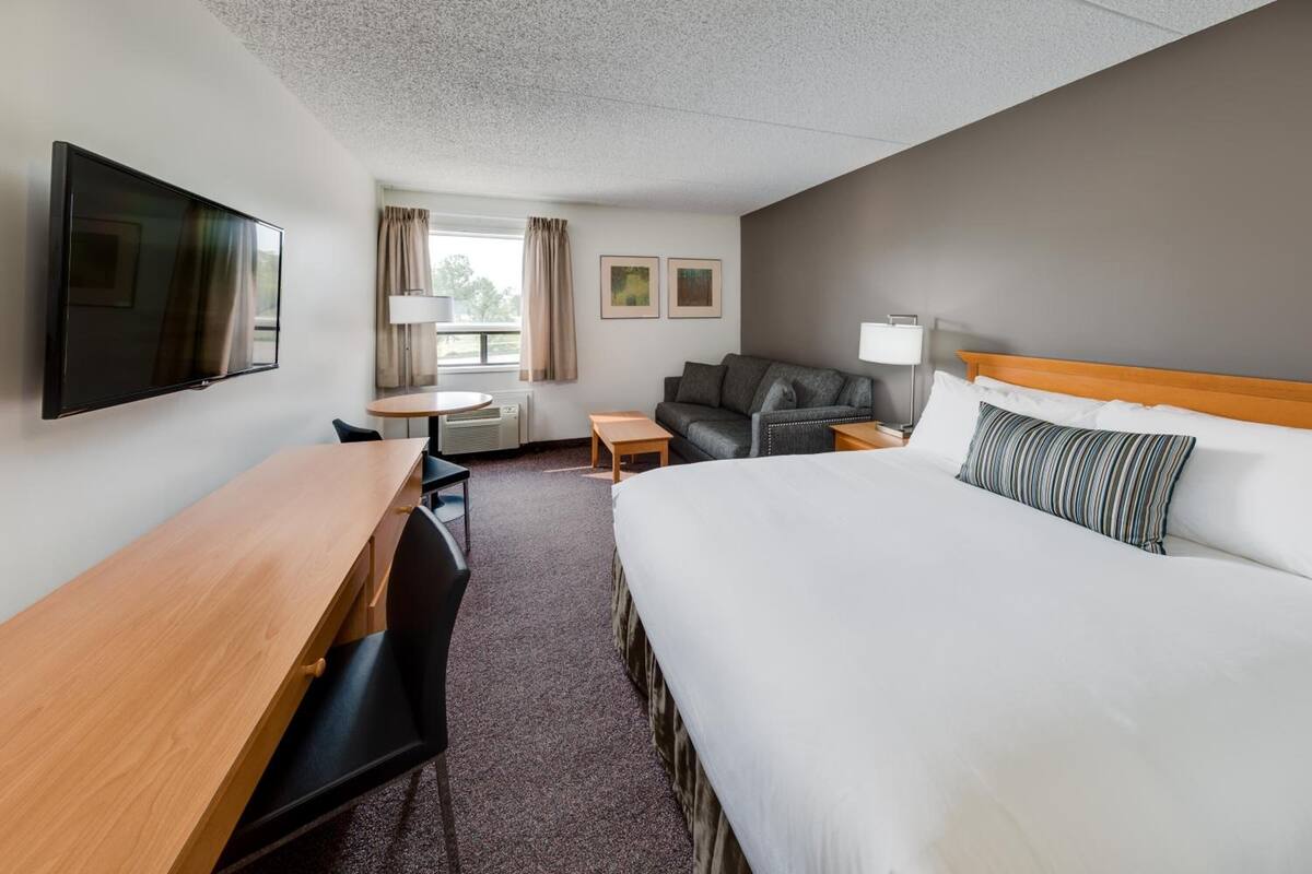 Une chambre d’hôtel comprenant un lit, un bureau, une chaise, un canapé, une télévision et une fenêtre avec des rideaux.