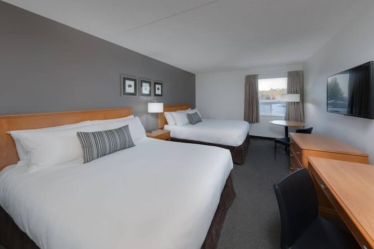 Une chambre d’hôtel avec deux lits, un bureau, une chaise, une télévision et une fenêtre avec des rideaux.