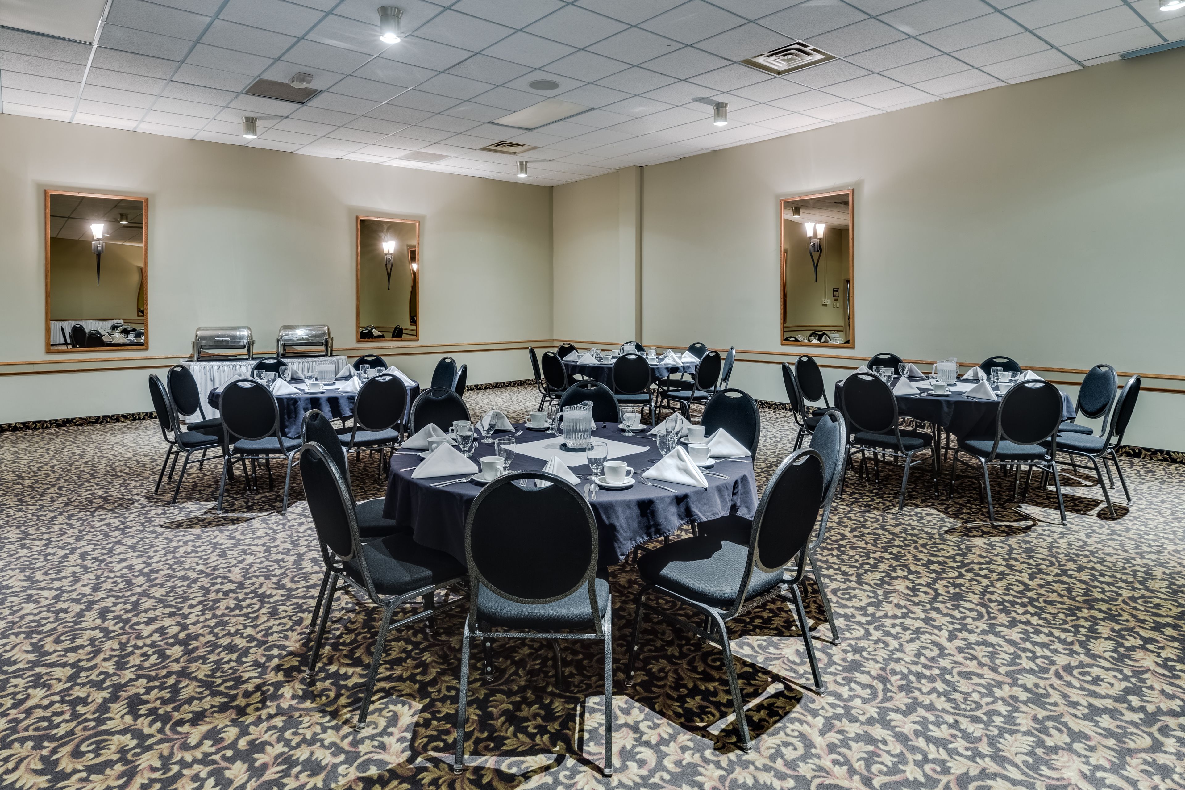 A conference room with round tables, black chairs, and a patterned carpet.