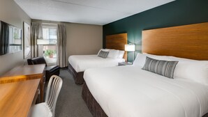 A hotel room with two beds, a desk, a chair, and a TV.
