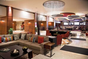 A modern lobby with a sectional sofa, armchairs, a coffee table, and a dining area. - Marriott Hotel Tijuana (Tijuana)
