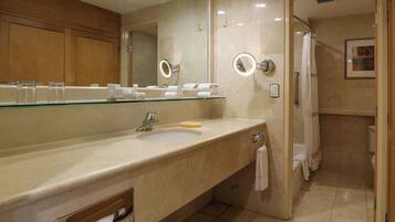 A modern bathroom with a glass-topped sink, a large mirror, and a shower area.